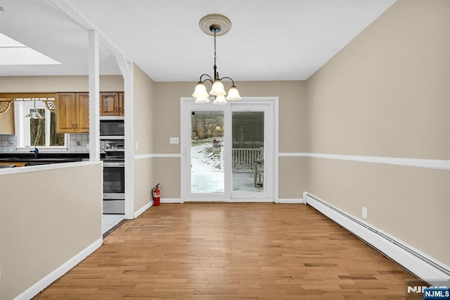 unfurnished dining area featuring an inviting chandelier, baseboard heating, and light hardwood / wood-style floors