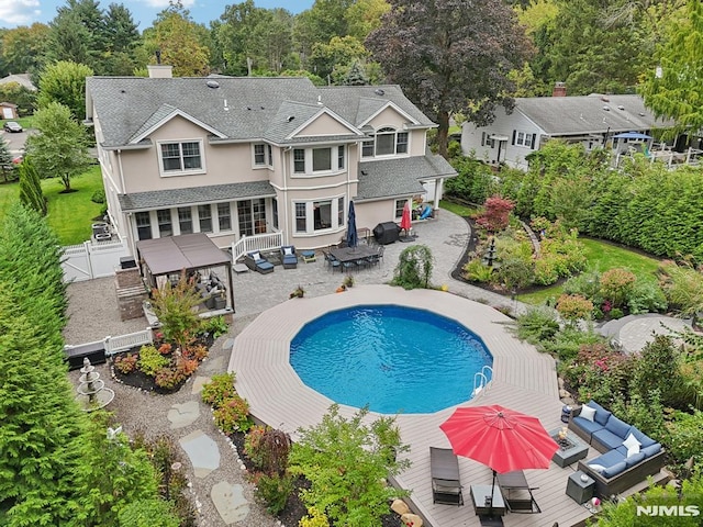 back of house with fence, driveway, a wooden deck, an outdoor pool, and a chimney