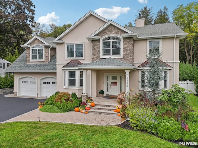 traditional-style house featuring a garage, stone siding, driveway, roof with shingles, and stucco siding