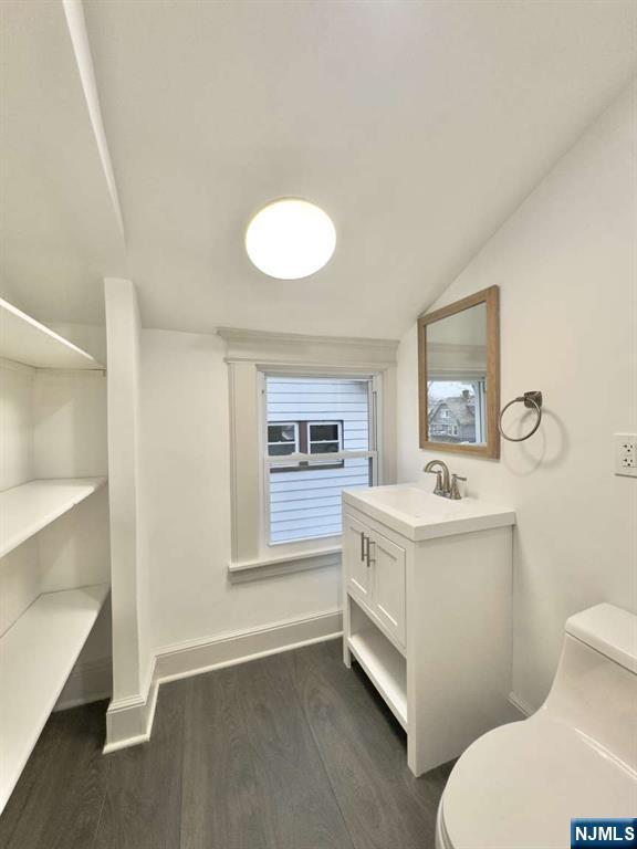 bathroom with wood-type flooring, vaulted ceiling, vanity, and toilet