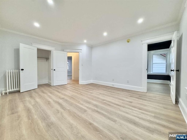 unfurnished bedroom featuring crown molding, radiator, light wood-type flooring, and a closet