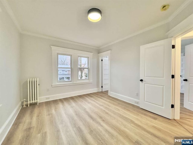 empty room with crown molding, radiator heating unit, and light hardwood / wood-style floors