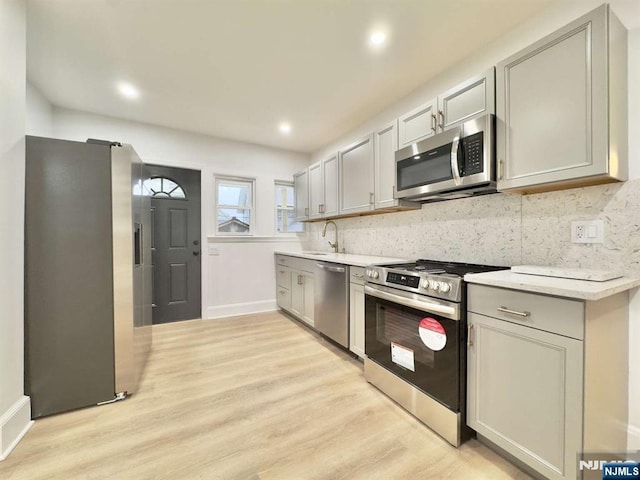 kitchen featuring sink, gray cabinetry, light hardwood / wood-style flooring, appliances with stainless steel finishes, and backsplash