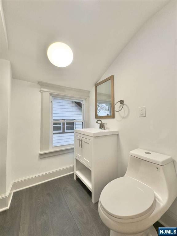 bathroom featuring wood-type flooring, lofted ceiling, vanity, and toilet