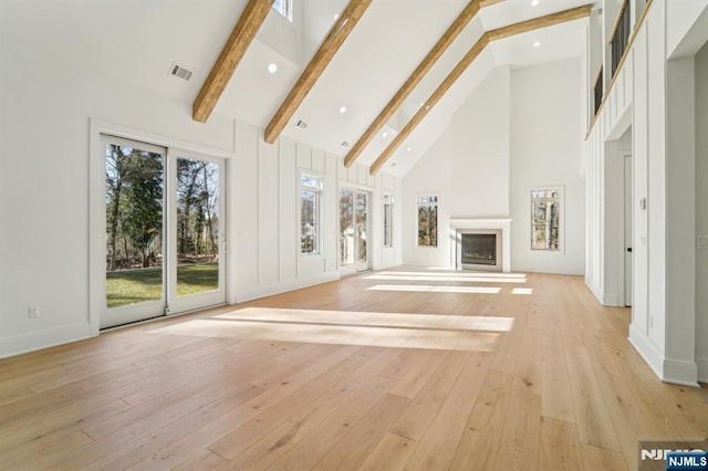 unfurnished living room featuring a skylight, high vaulted ceiling, light hardwood / wood-style floors, and beamed ceiling