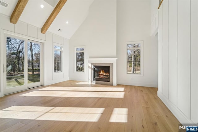 unfurnished living room featuring a healthy amount of sunlight, light hardwood / wood-style flooring, high vaulted ceiling, and beamed ceiling