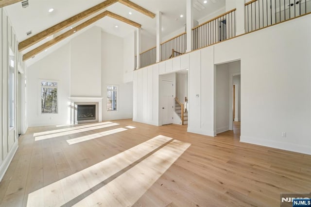 unfurnished living room featuring high vaulted ceiling, light hardwood / wood-style floors, and beamed ceiling