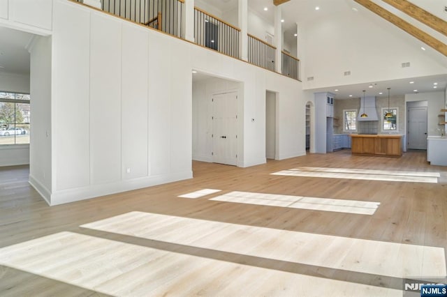 unfurnished living room with a towering ceiling, beam ceiling, and light hardwood / wood-style flooring