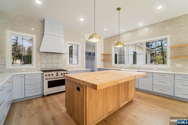 kitchen with butcher block countertops, custom exhaust hood, range with gas cooktop, decorative light fixtures, and a kitchen island