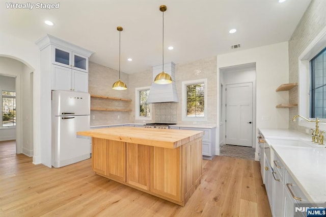 kitchen with white fridge, a center island, white cabinets, and wood counters