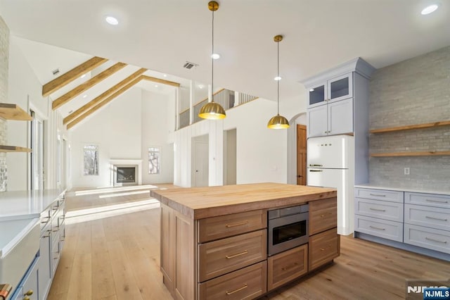 kitchen with wooden counters, hanging light fixtures, light wood-type flooring, stainless steel microwave, and backsplash