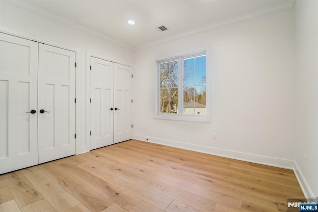 unfurnished bedroom featuring crown molding, two closets, and light hardwood / wood-style flooring