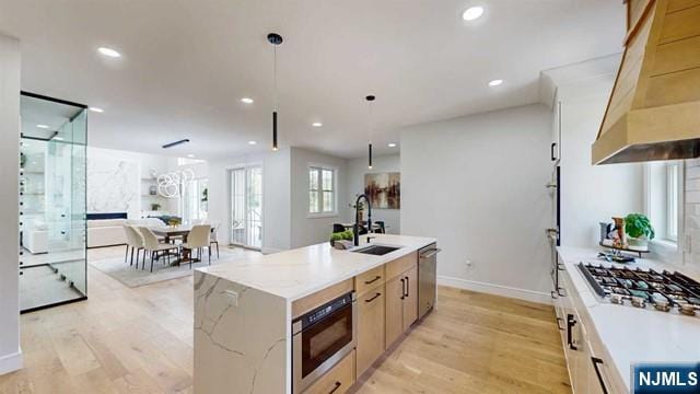 kitchen with appliances with stainless steel finishes, extractor fan, light wood-type flooring, and a sink