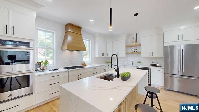 kitchen featuring light wood-style flooring, premium range hood, a sink, appliances with stainless steel finishes, and open shelves