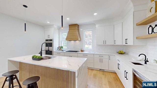 kitchen featuring double oven, premium range hood, a sink, and open shelves