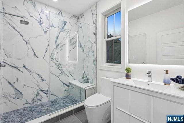 full bath with a marble finish shower, vanity, and toilet