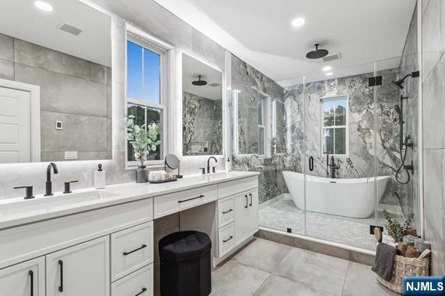 bathroom with a stall shower, a sink, tile walls, and double vanity