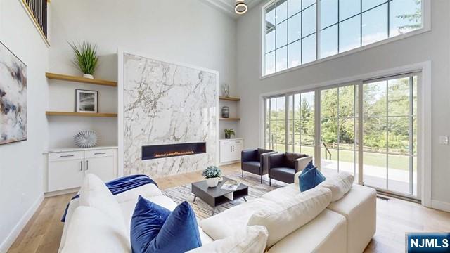 living area featuring a high end fireplace, baseboards, a high ceiling, and wood finished floors