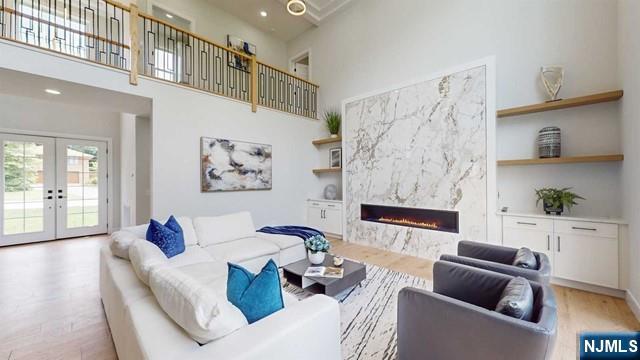 living room featuring a high ceiling, a high end fireplace, wood finished floors, and french doors