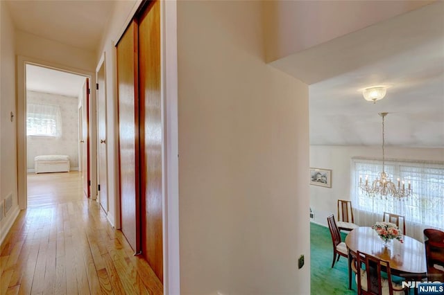 corridor featuring light wood-style floors, visible vents, and an inviting chandelier