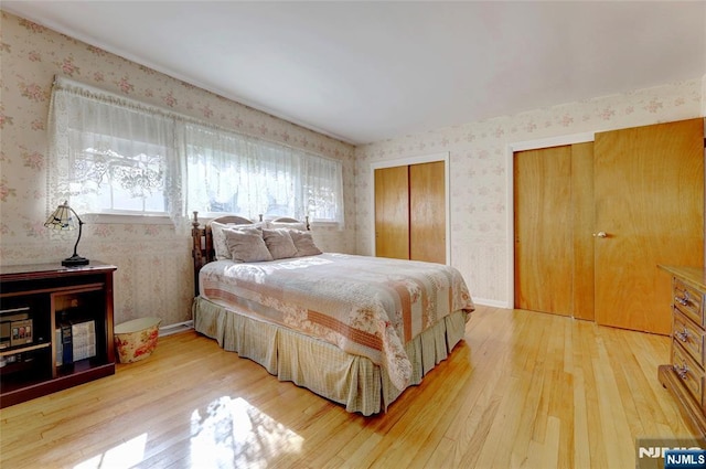 bedroom featuring multiple closets, light wood finished floors, and wallpapered walls