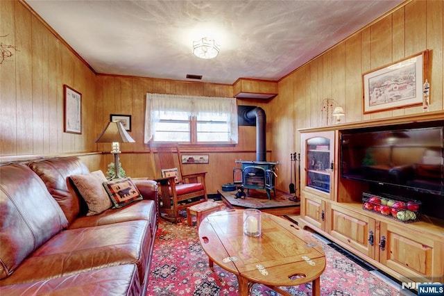 living room featuring visible vents, wood finished floors, a wood stove, and crown molding