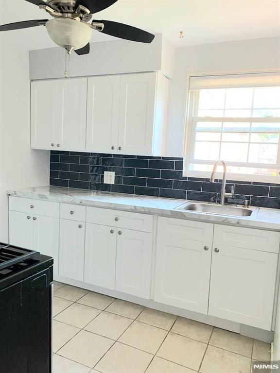 kitchen featuring black range oven, sink, backsplash, and white cabinets