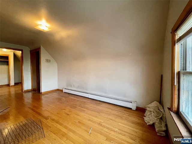 unfurnished room featuring a baseboard heating unit, a wealth of natural light, light hardwood / wood-style flooring, and vaulted ceiling