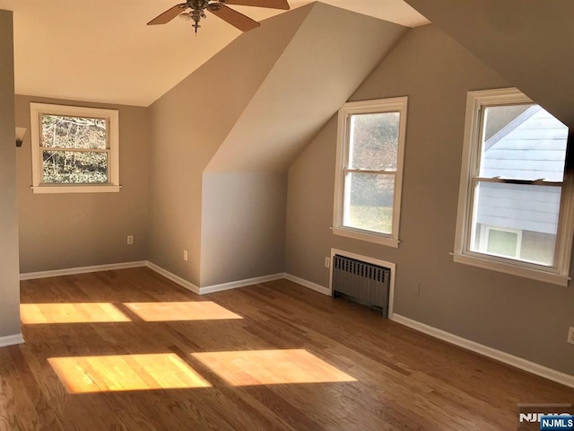 additional living space with radiator, hardwood / wood-style flooring, vaulted ceiling, and ceiling fan