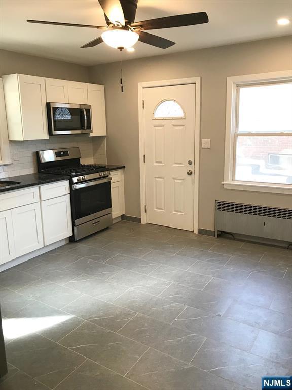 kitchen featuring white cabinets, stainless steel appliances, decorative backsplash, and radiator heating unit