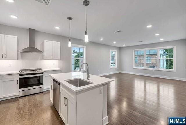 kitchen featuring sink, appliances with stainless steel finishes, white cabinetry, a center island with sink, and wall chimney exhaust hood