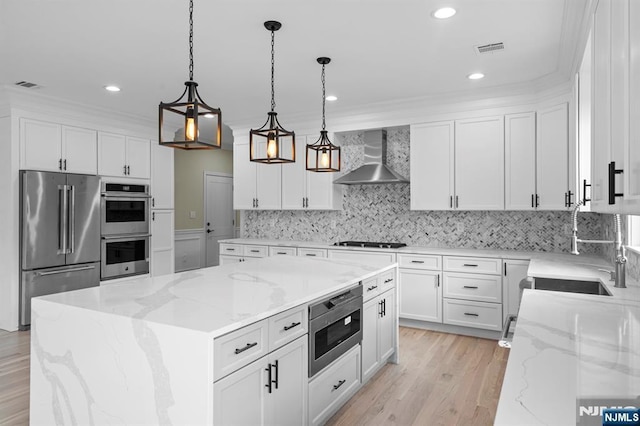 kitchen featuring a center island, hanging light fixtures, wall chimney range hood, stainless steel appliances, and white cabinets