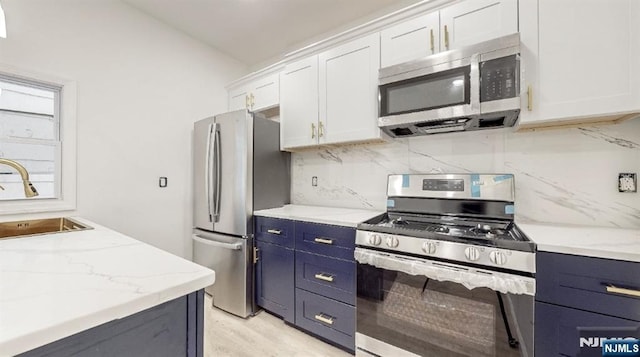 kitchen featuring appliances with stainless steel finishes, sink, white cabinets, decorative backsplash, and light stone countertops