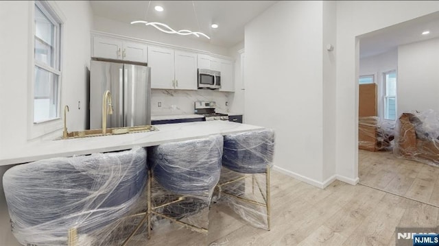 kitchen with appliances with stainless steel finishes, white cabinets, decorative backsplash, light stone counters, and light wood-type flooring