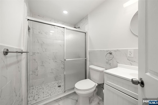 bathroom with vanity, a shower with shower door, tile walls, and toilet