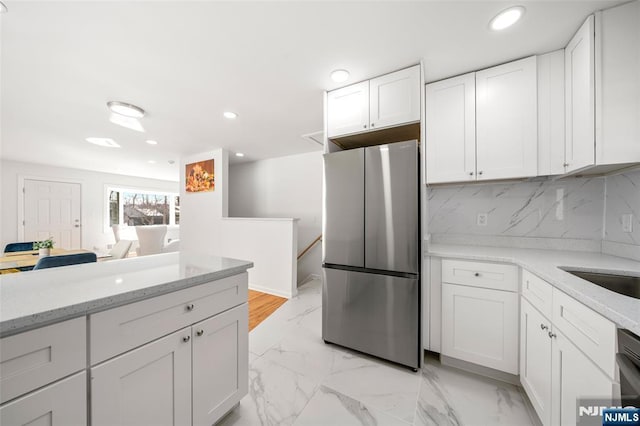 kitchen with white cabinets, light stone countertops, stainless steel fridge, and decorative backsplash