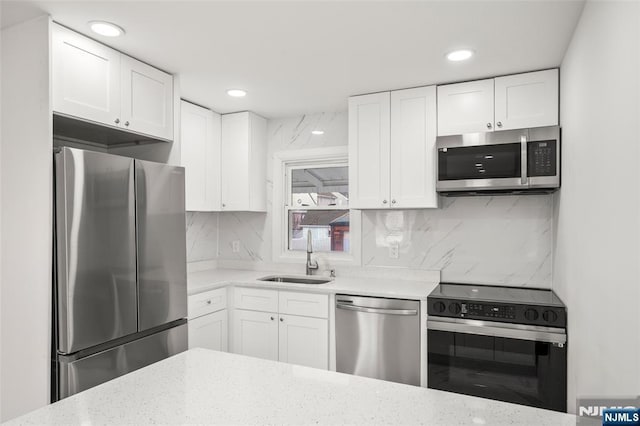 kitchen featuring sink, white cabinetry, stainless steel appliances, light stone countertops, and backsplash