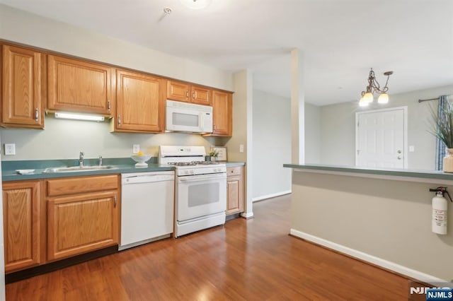 kitchen featuring dark wood finished floors, white appliances, decorative light fixtures, and a sink