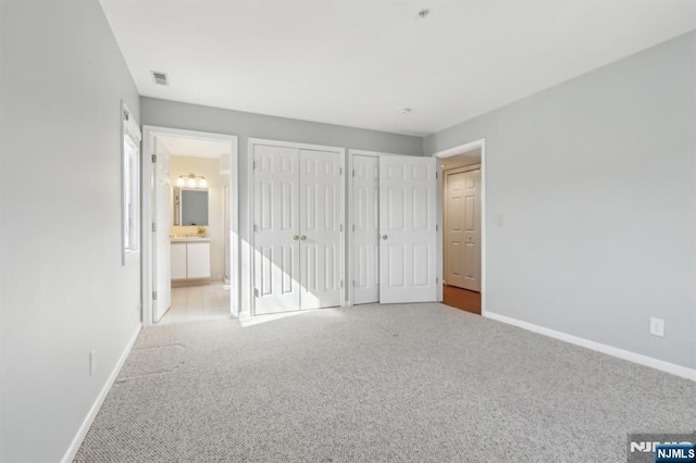 unfurnished bedroom with baseboards, multiple closets, visible vents, and light colored carpet