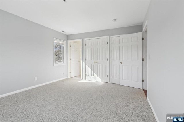 unfurnished bedroom featuring carpet, baseboards, and multiple closets