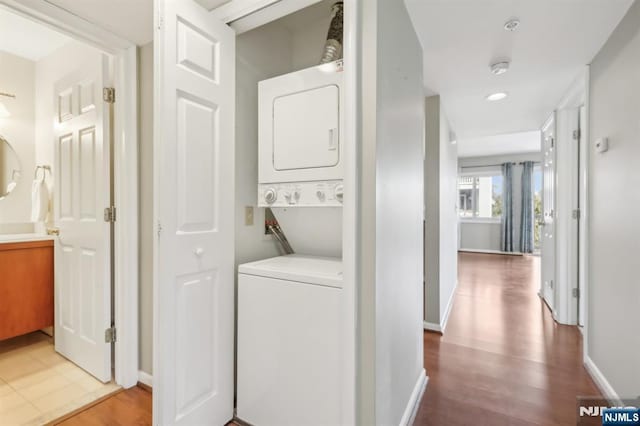 laundry room with laundry area, stacked washing maching and dryer, wood finished floors, and baseboards