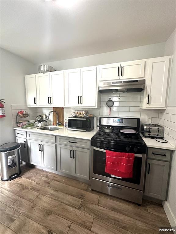 kitchen with dark wood-type flooring, sink, gas stove, white cabinetry, and decorative backsplash