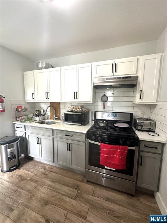 kitchen featuring sink, stainless steel gas stove, dark hardwood / wood-style flooring, decorative backsplash, and white cabinets