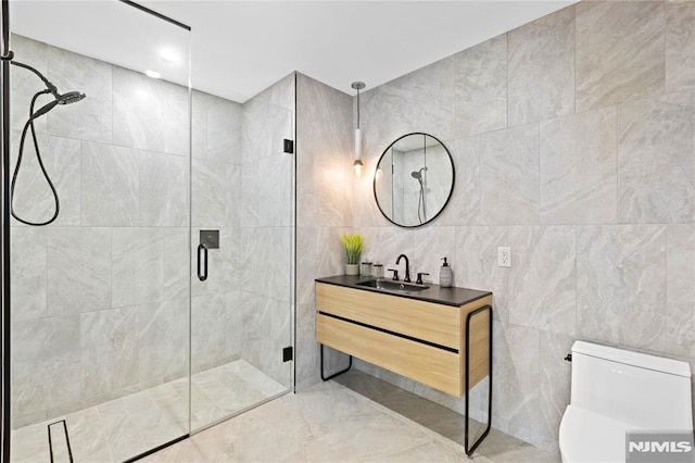 bathroom featuring vanity, toilet, a shower with door, and tile walls