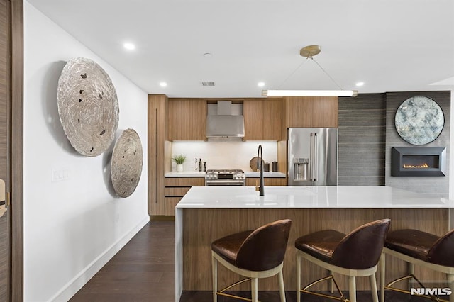 kitchen featuring a large fireplace, dark hardwood / wood-style flooring, high end appliances, kitchen peninsula, and wall chimney exhaust hood