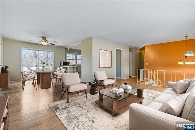 living room with rail lighting, ceiling fan with notable chandelier, and light hardwood / wood-style floors