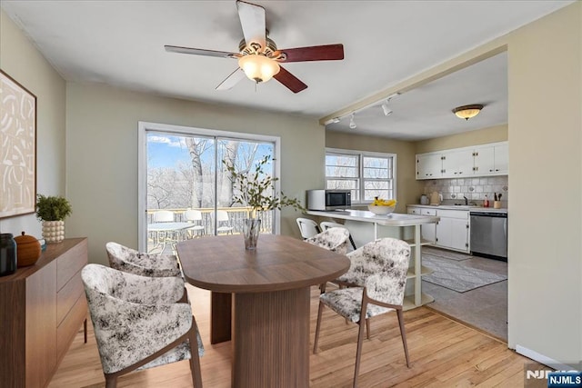 dining room with ceiling fan, rail lighting, sink, and light wood-type flooring