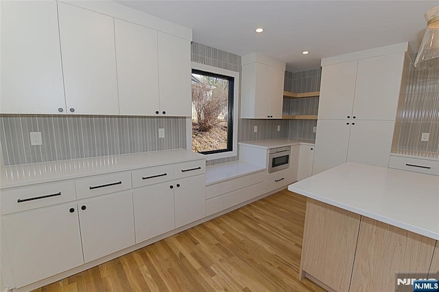 kitchen with white cabinets, light countertops, light wood-type flooring, open shelves, and stainless steel microwave