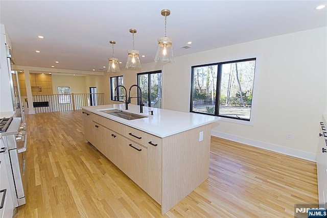 kitchen featuring an island with sink, light countertops, light wood-type flooring, a sink, and recessed lighting