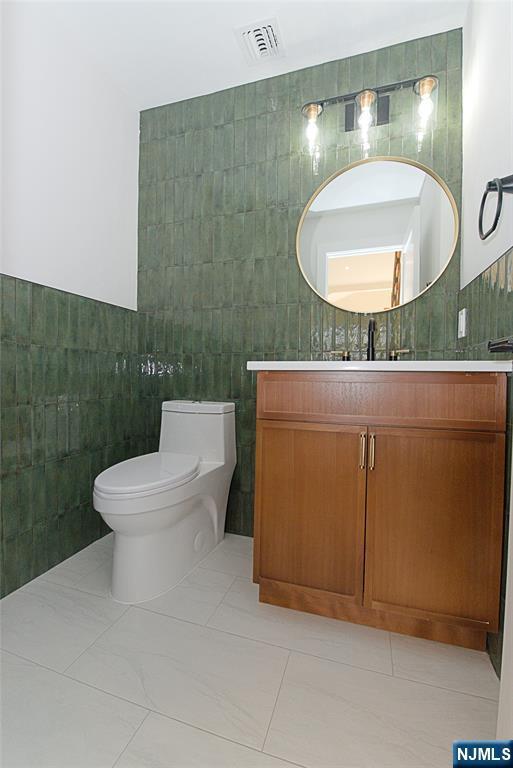 bathroom featuring visible vents, tile walls, toilet, and vanity